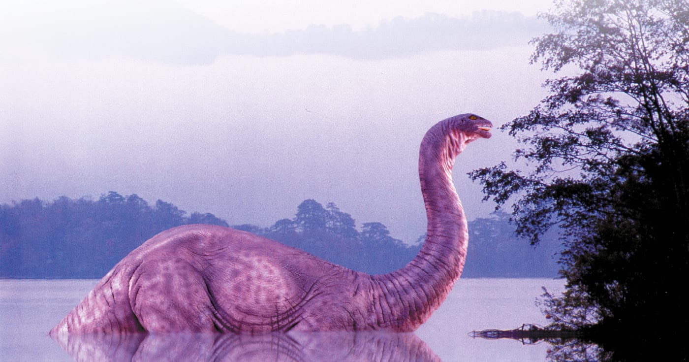 Dinosaurus järvessä, osa vartalosta vedenpinnan alapuolella, rannalla puustoa. Kuva ©: Robert Jensen